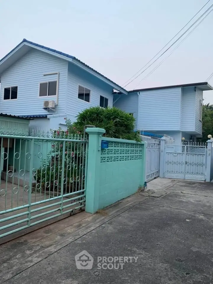Charming blue two-story house with gated entrance and lush greenery.