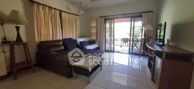 Spacious living room with cozy seating and large windows opening to a balcony with lush views.