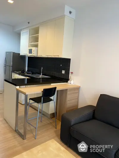 Modern studio apartment with a sleek kitchen featuring a gas stove and black tile backsplash, complemented by a cozy living area with a comfortable sofa.