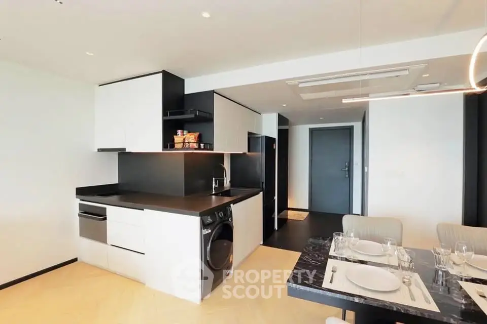 Modern kitchen with sleek black and white design, featuring built-in appliances and dining area.