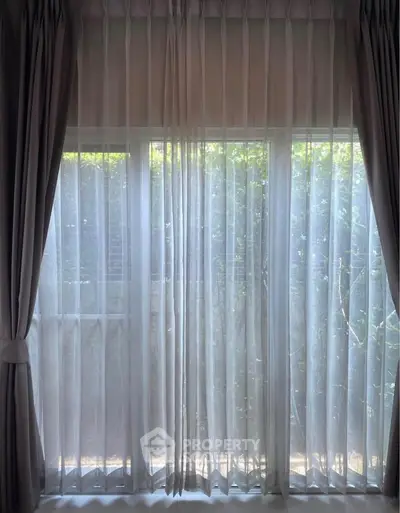 Elegant window with sheer curtains offering a serene garden view, perfect for natural light lovers.