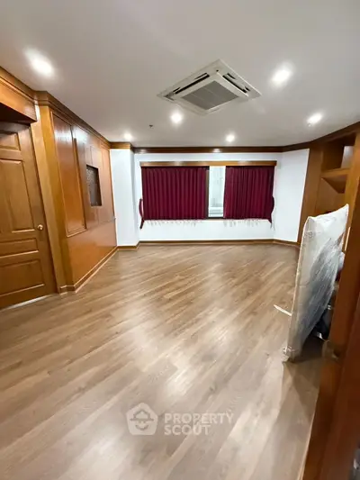 Spacious empty room with wooden flooring and red curtains, ideal for customization.