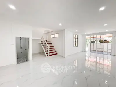 Spacious modern living room with glossy floors and staircase, abundant natural light.