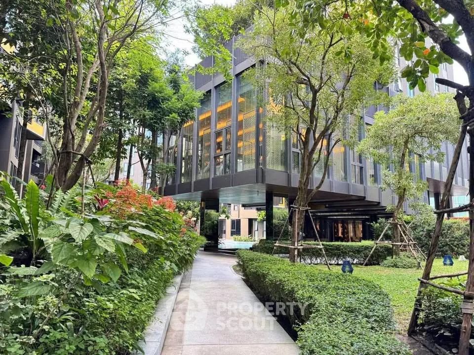 Modern building exterior with lush garden and pathway, showcasing contemporary architecture and greenery.