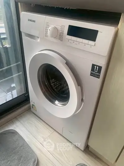 Modern washing machine in a stylish laundry area with natural light and sleek flooring.