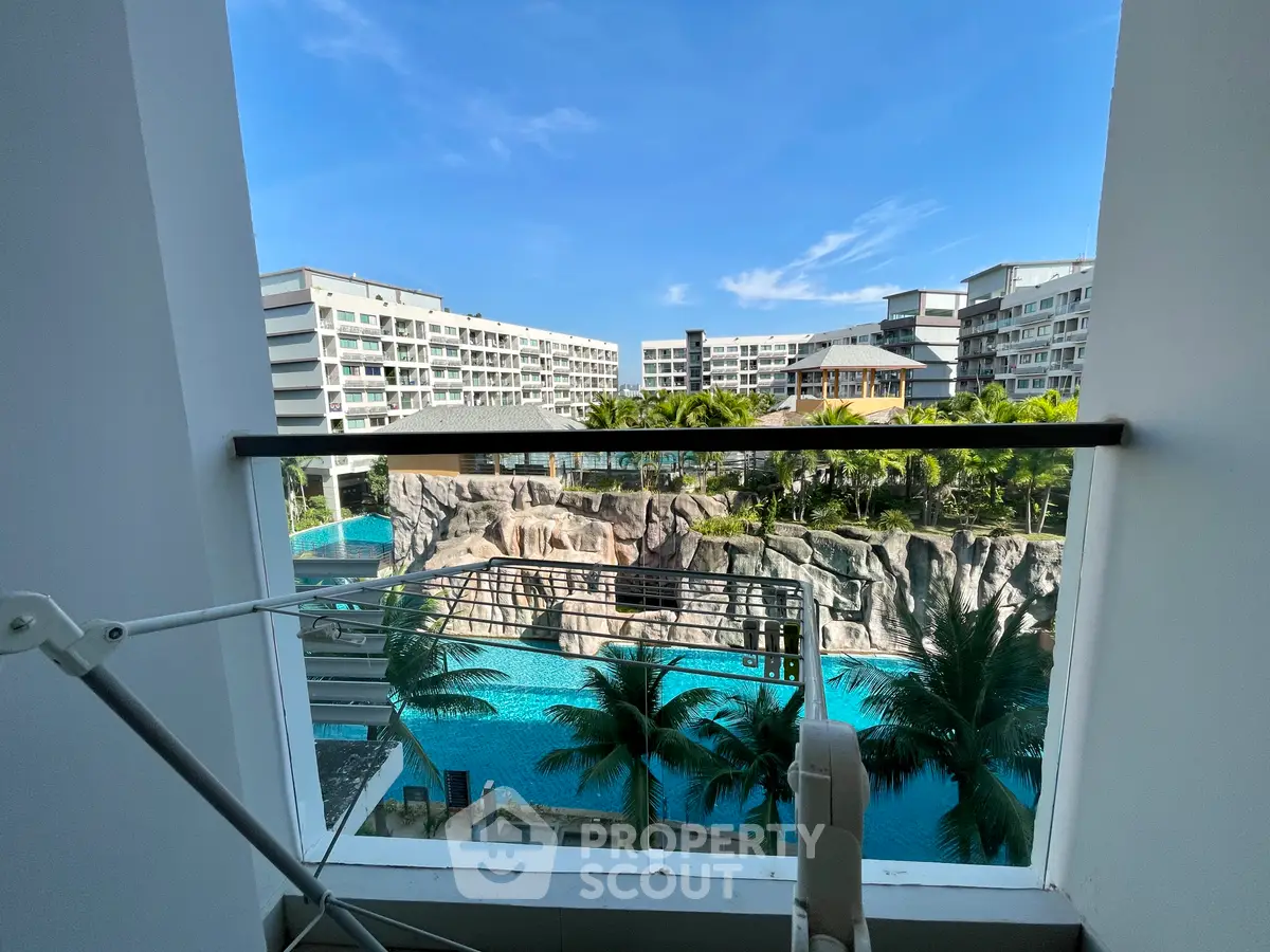Stunning balcony view of resort-style pool and modern buildings under clear blue sky.