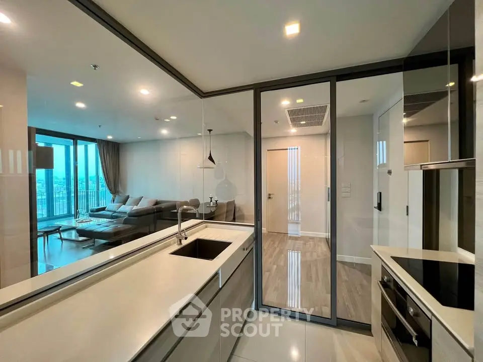 Modern open-layout kitchen with sleek design and spacious living area, featuring large windows and contemporary furnishings.
