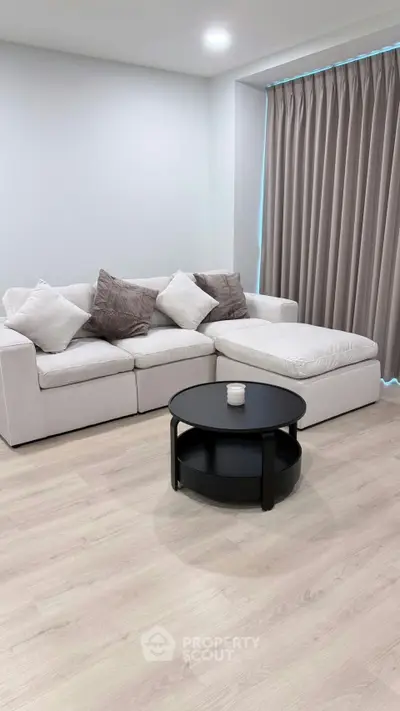Modern living room with white sectional sofa and round black coffee table on light wood flooring.