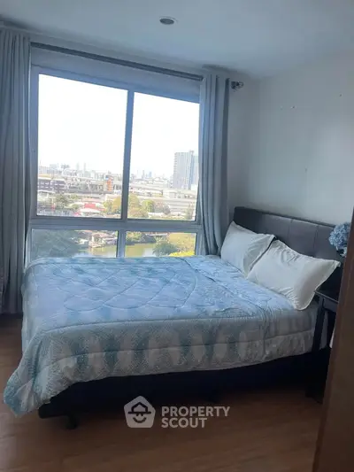 Cozy bedroom with large window offering stunning city view, perfect for relaxation and comfort.