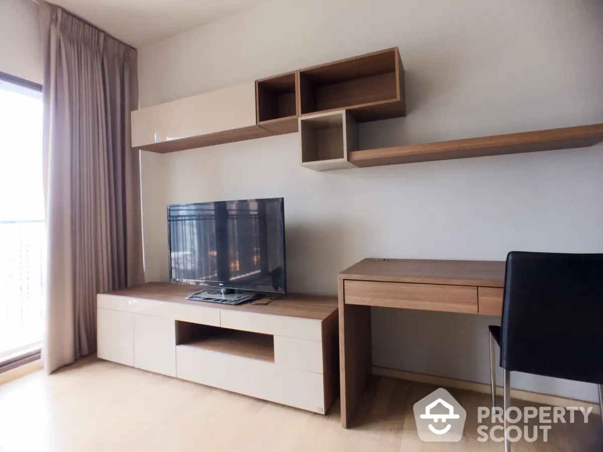 Spacious and well-lit living room with modern wooden furniture, including a sleek TV stand and floating shelves, complemented by a large window.