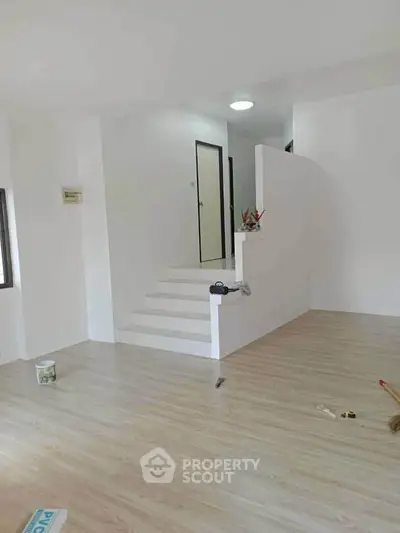 Spacious modern interior with wooden flooring and white walls, featuring a small staircase.