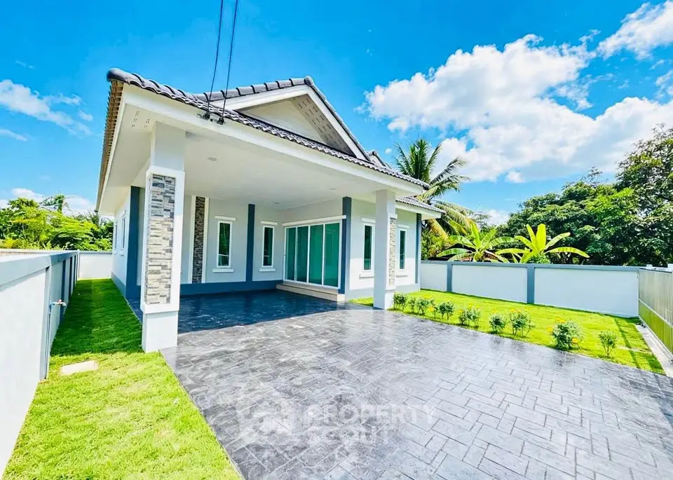 Modern single-story house with spacious driveway and lush garden under a clear blue sky.