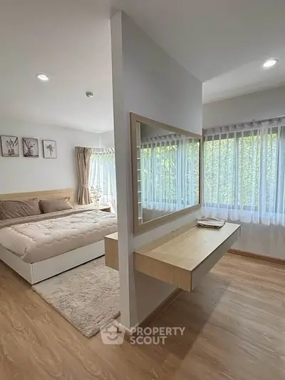 Spacious bedroom with large windows and elegant decor, featuring a cozy bed and a stylish vanity area.