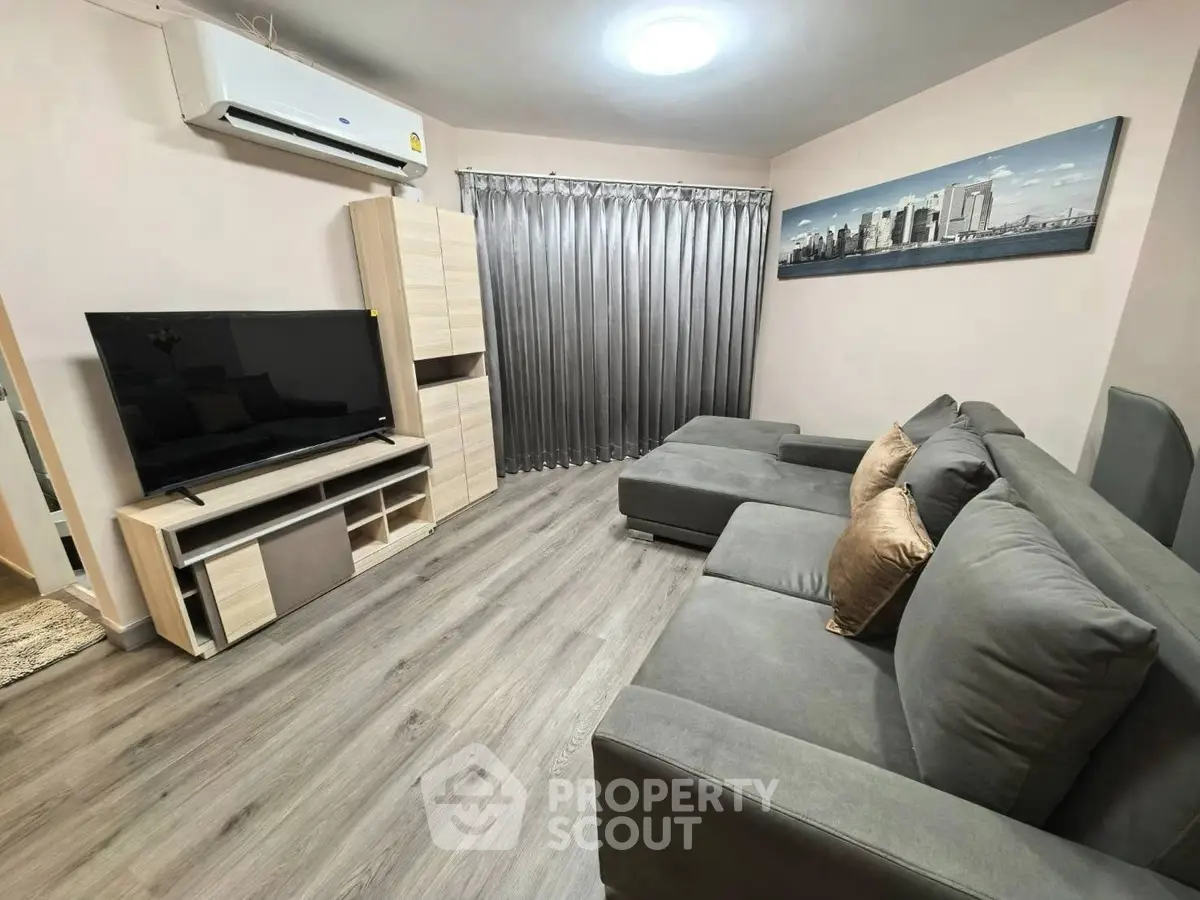 Modern living room with sleek gray sofa and entertainment center, featuring stylish decor and wood flooring.