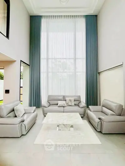 Luxurious high-ceiling living room with elegant gray sofas and floor-to-ceiling windows.