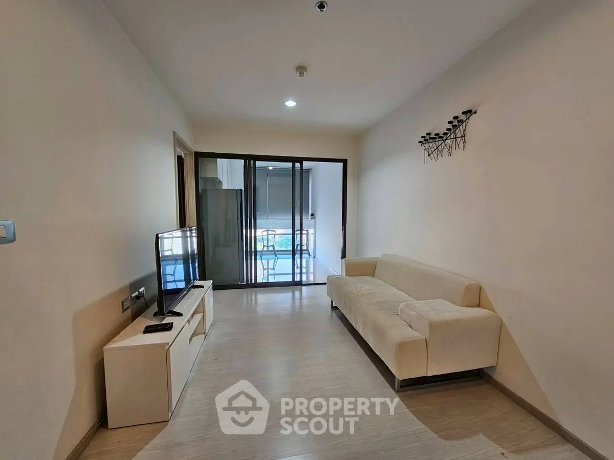 Modern living room with sleek design and balcony access, featuring a comfortable sofa and flat-screen TV.