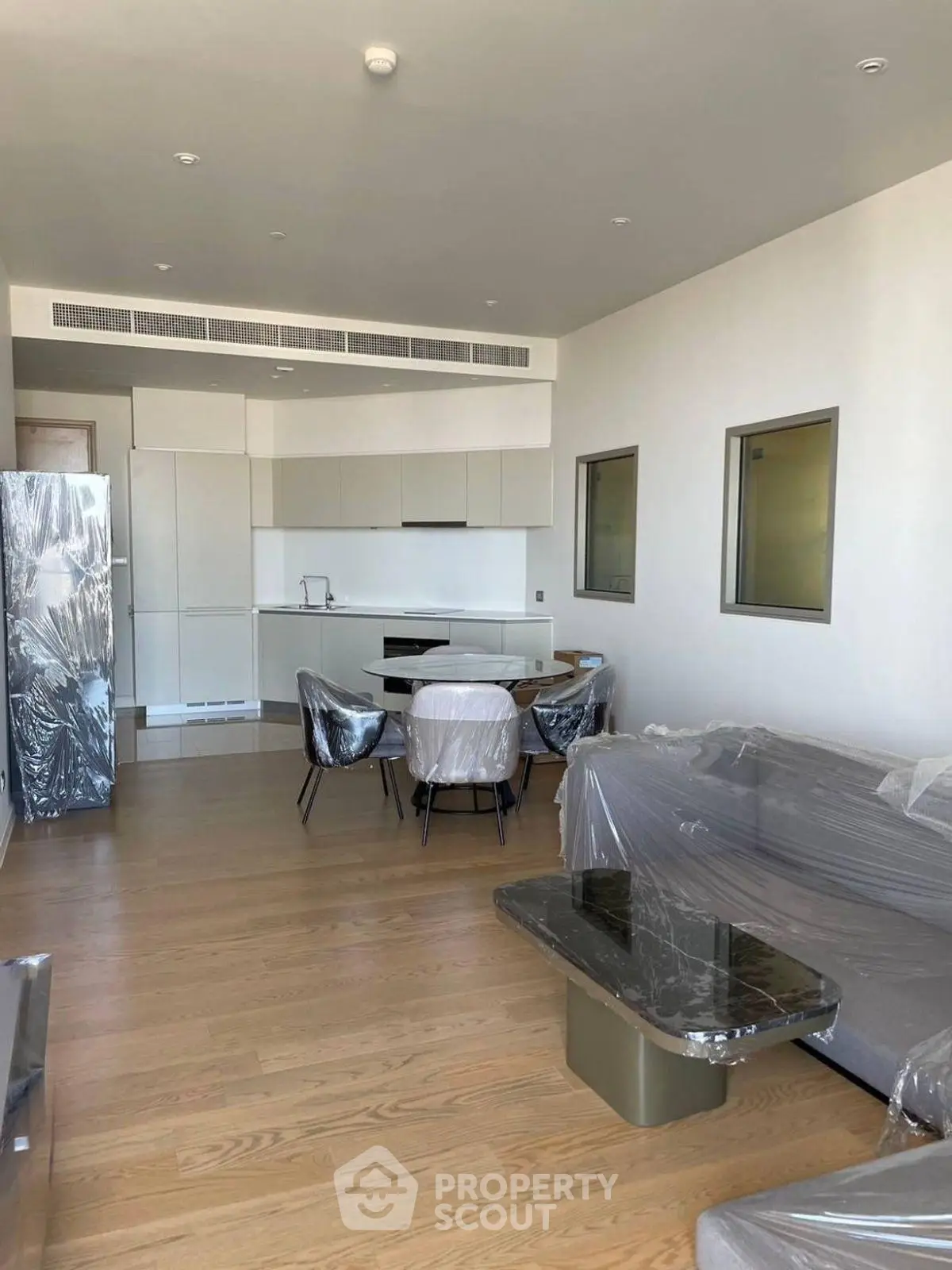 Modern open-layout living room with kitchen, featuring sleek furniture and wooden flooring.