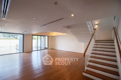 Spacious open-plan living room with wooden flooring and staircase, ideal for modern living.
