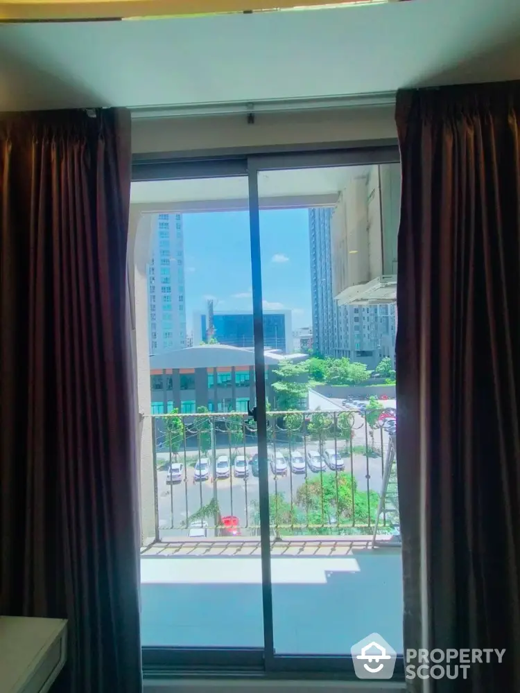 Bright city view from apartment balcony with sliding glass doors and curtains.