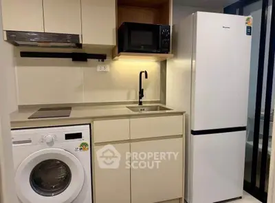 Modern compact kitchen with washing machine, fridge, and microwave in sleek apartment.