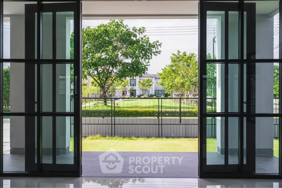 Spacious modern entrance with glass doors opening to lush green garden view.