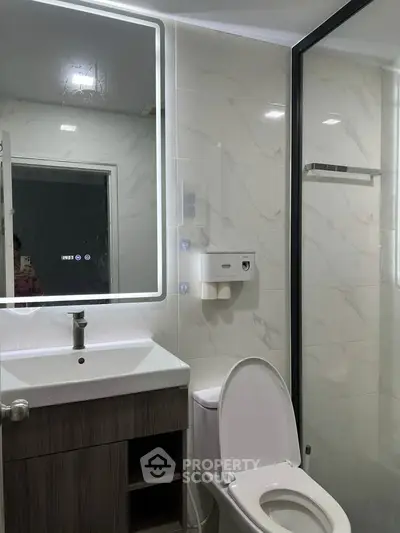 Modern bathroom with sleek design, featuring a backlit mirror and glass shower enclosure.