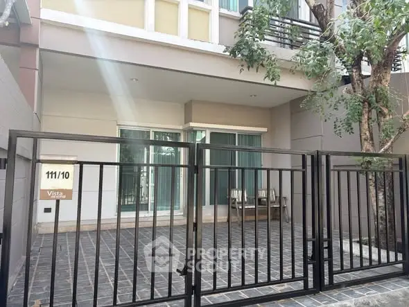 Modern townhouse entrance with sleek black gate and tree-lined patio.
