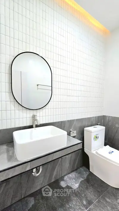 Modern bathroom with sleek design, featuring a stylish oval mirror and contemporary fixtures.