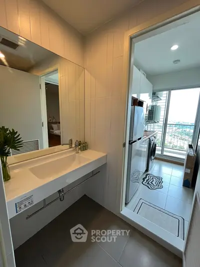 Modern bathroom with sleek design and view into a bright kitchen with balcony access.