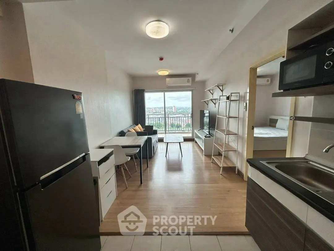 Modern open-plan living room with kitchen, featuring sleek appliances and a city view balcony.