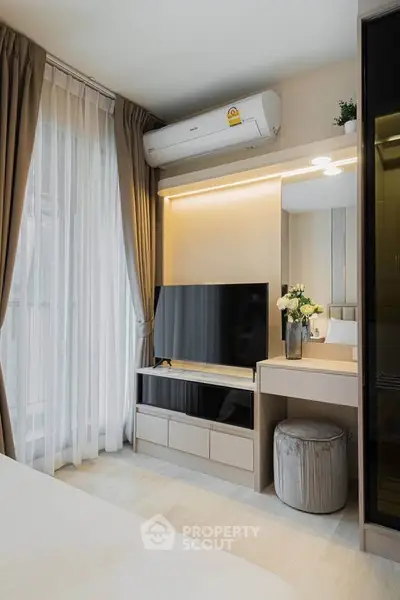 Modern bedroom with sleek TV setup and elegant decor, featuring a large window with sheer curtains.