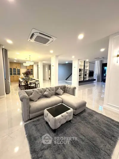 Luxurious open-plan living room with plush gray sofa and elegant dining area, perfect for modern family living.
