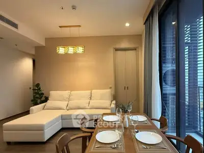 Modern living room with elegant dining area and cozy sofa, featuring large windows for natural light.