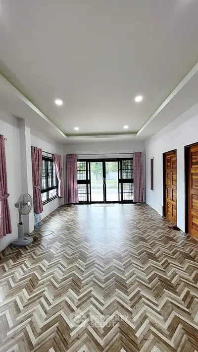 Spacious living room with elegant herringbone flooring and large windows for natural light.