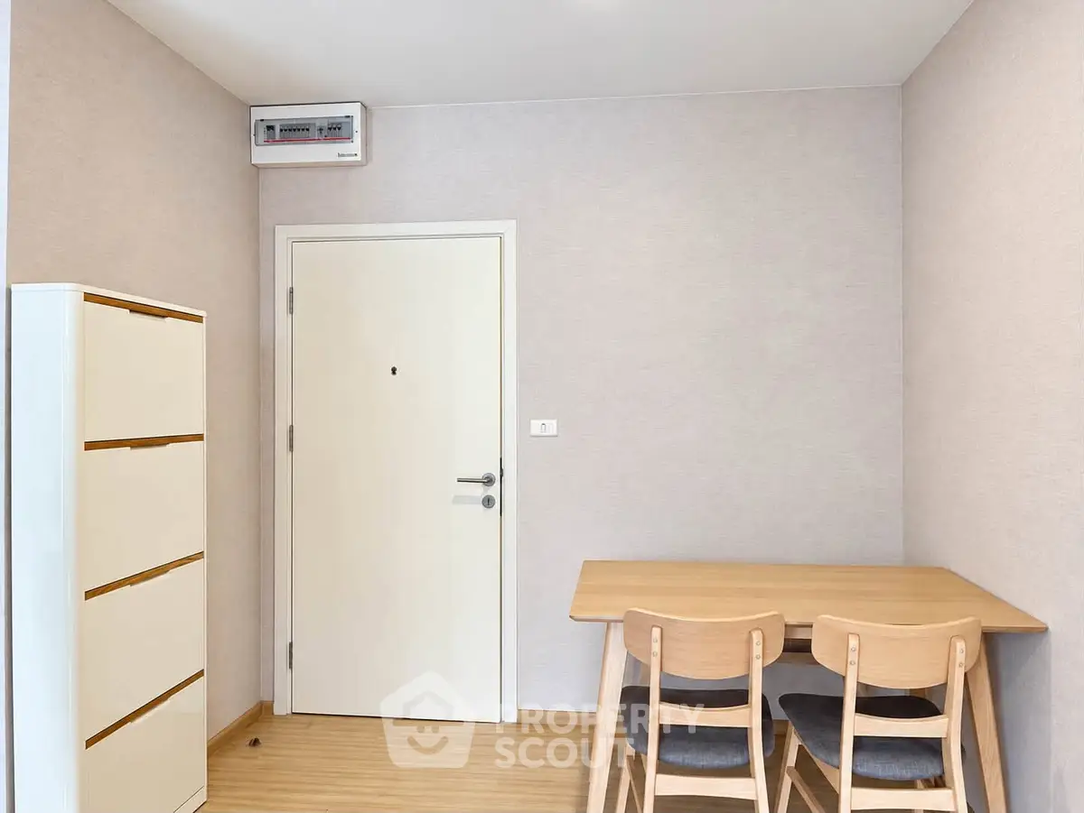 Cozy minimalist dining area with wooden table and chairs, adjacent to a sleek white door and storage unit.
