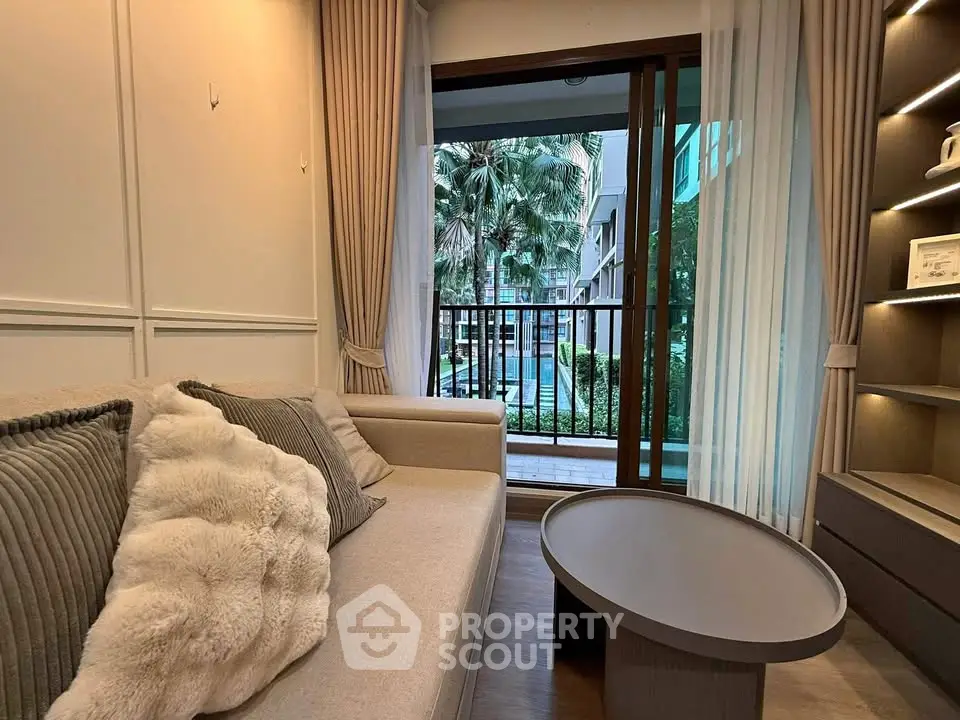Cozy living room with modern decor and balcony view of lush greenery.