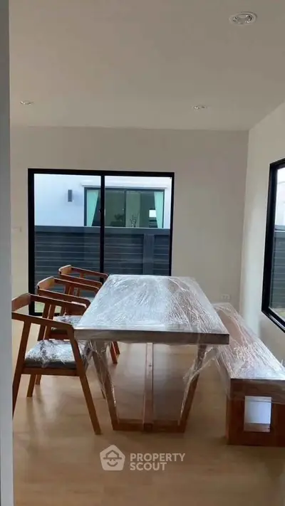 Modern dining area with wooden table and chairs, large windows, and natural light.