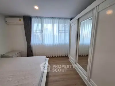 Spacious bedroom with large window and elegant wardrobe in modern apartment.