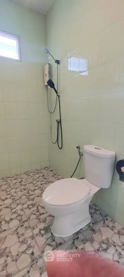 Modern bathroom with tiled walls and floor, featuring a toilet and shower area.