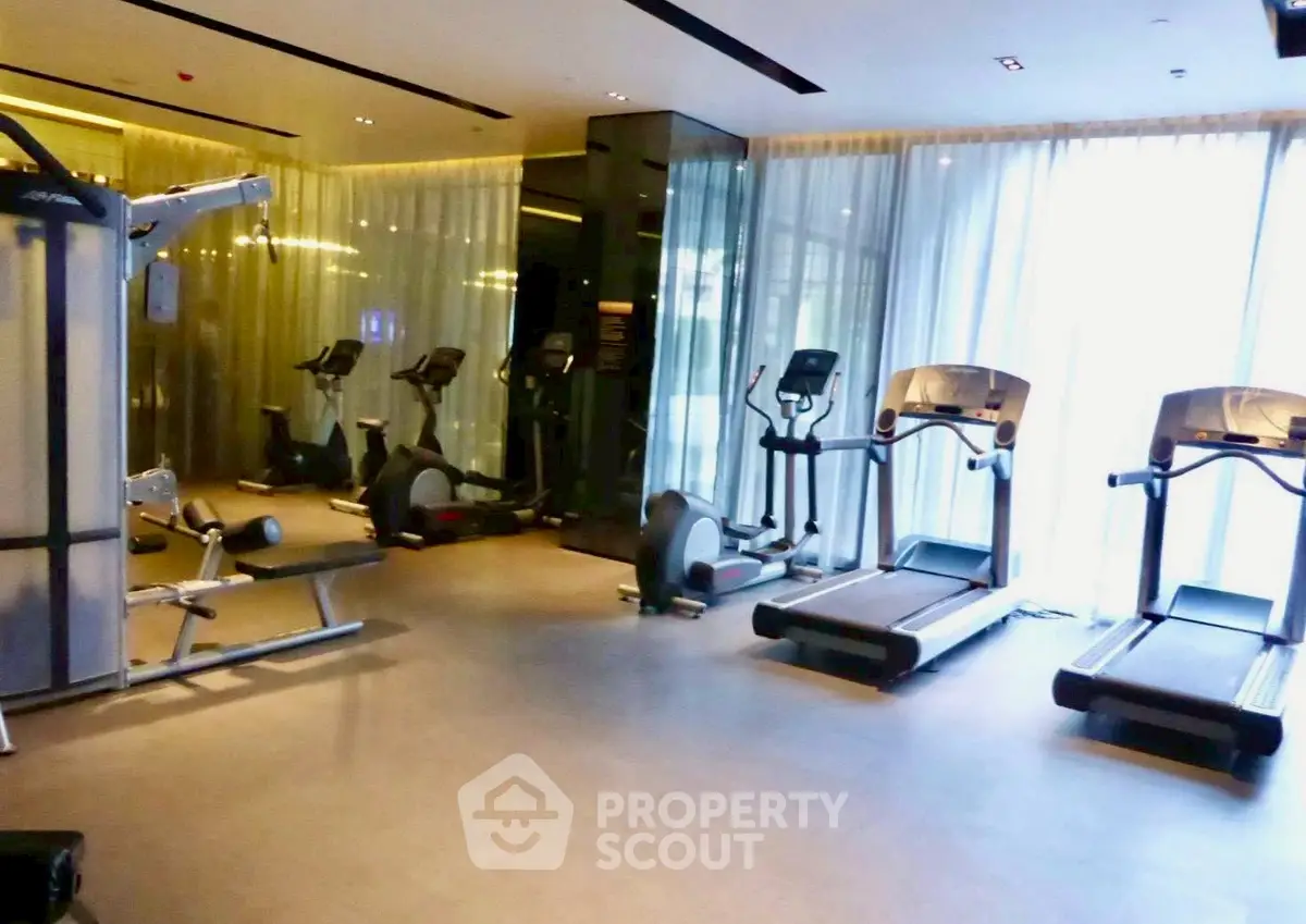 Modern gym with state-of-the-art equipment and floor-to-ceiling windows in luxury building.