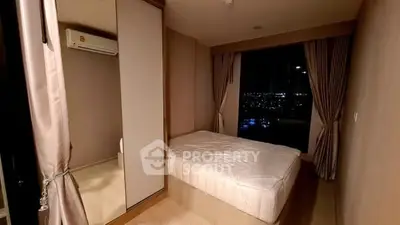 Cozy bedroom with city view, featuring large window and modern decor.
