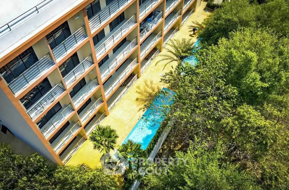 Stunning aerial view of modern apartment building with lush greenery and inviting pool.