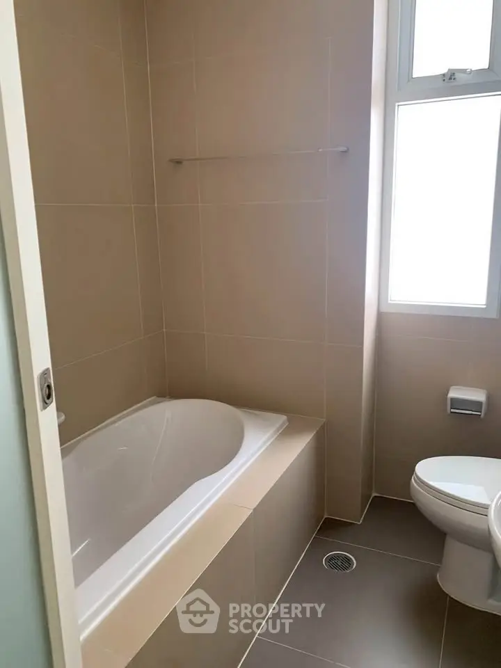 Modern bathroom with bathtub and natural light from window.