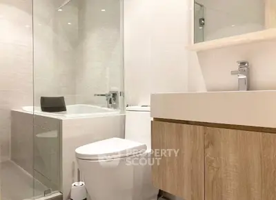 Modern bathroom with sleek fixtures and glass-enclosed bathtub in contemporary apartment.