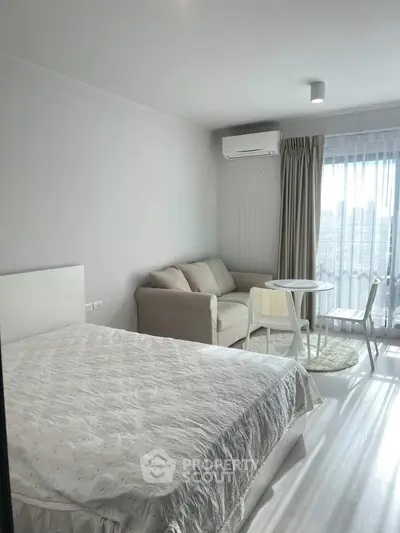 Bright modern studio apartment with cozy bed, compact dining area, and large window for natural light.