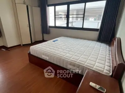 Spacious bedroom with large window and wooden flooring, featuring a comfortable bed and ample storage space.