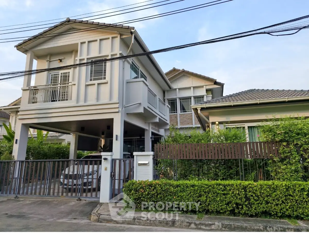 Charming two-story house with lush greenery and gated entrance in a serene neighborhood.