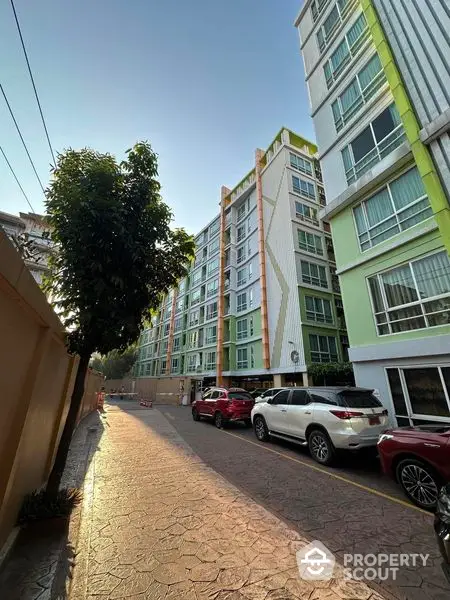 Modern apartment building exterior with parked cars and tree-lined pathway