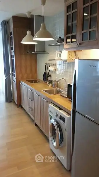Modern kitchen with wooden cabinets, washing machine, and stainless steel fridge