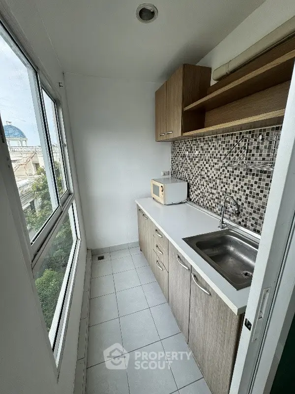 Compact kitchen with mosaic backsplash and large window offering city views